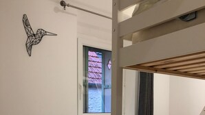 A bunk bed room with a window, a wall-mounted light fixture, and a geometric wall art piece. - Charming seaside house with enclosed garden (Bernières-sur-Mer)