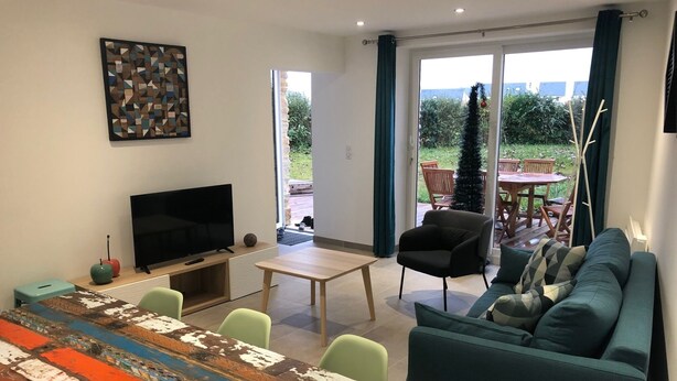 A modern living room with a television, a coffee table, a sofa, and a dining area with chairs. - Charming seaside house with enclosed garden (Bernières-sur-Mer)