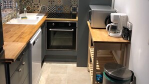 A modern kitchen with a wooden countertop, a built-in oven, a coffee maker, and a trash bin. - Charming seaside house with enclosed garden (Bernières-sur-Mer)