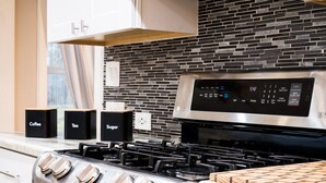 A kitchen with a stainless steel stove, a black tiled backsplash, and white cabinetry. - Retreat in the woods! (Houston)