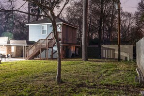 A two-story house with a wooden staircase leading to a deck, surrounded by trees and a fenced yard.