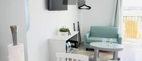 Ein modernes Hotelzimmer mit weißem Schreibtisch, einem runden Tisch, einer Couch und einem an der Wand befestigten Fernseher.