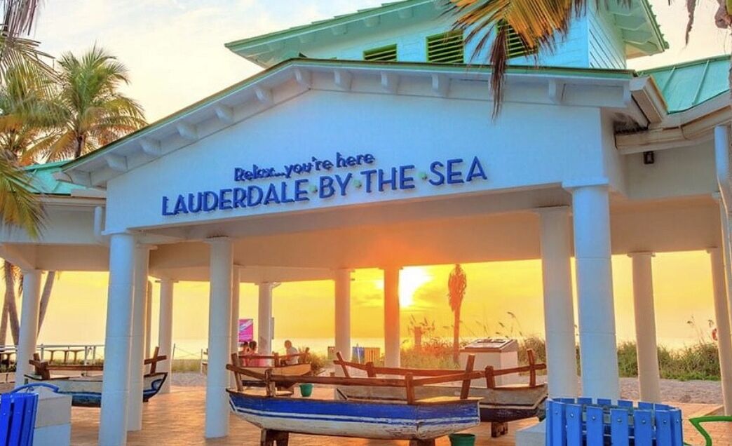 A beachside pavilion with a sign reading "Relax...you're here LAUDERDALE BY THE SEA".