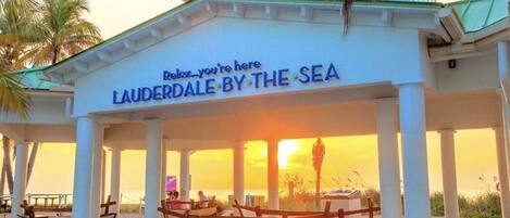 A beachside pavilion with a sign reading "Relax...you're here LAUDERDALE BY THE SEA".