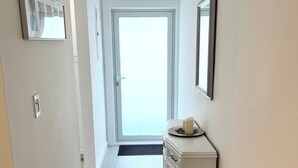 A hallway with a white door, a white cabinet with a tray of items, and a framed picture on the wall.