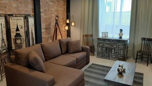Un salón con un sofá marrón, una mesa de centro de madera y una pared de ladrillo decorada con carteles.