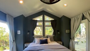 Ein Schlafzimmer mit einem großen Bett, zwei Nachttischen, einem Fenster mit Vorhängen und Blick auf Grünfläche.
