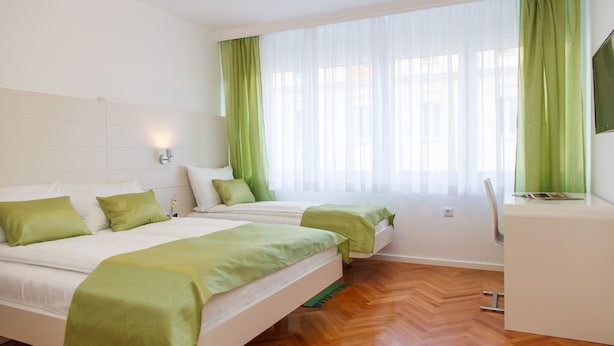A hotel room with two beds, a desk, and a large window with green curtains. - Apartment Jovanova (Belgrade)