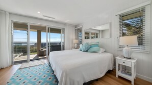 Un dormitorio con una cama grande, una mesita de noche, una lámpara y vistas al exterior a través de una puerta corrediza.