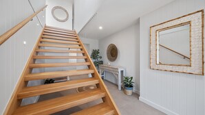Una escalera de madera con barandilla, un espejo redondo en la pared y un espejo decorativo con marco de bambú.