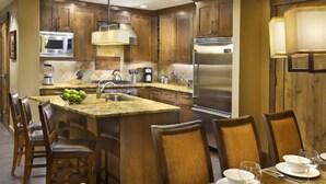 A modern kitchen with wooden cabinets, stainless steel appliances, and a dining area with chairs and a table set for four. - Stay and Ski in Northstar Resort (Truckee)