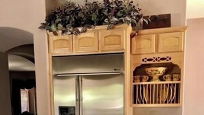 Una cucina con piano di lavoro in granito, frigorifero in acciaio inossidabile, mobili in legno e una pianta decorativa sopra.