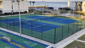 A tennis court with a net, surrounded by a fence, and adjacent to a building. - Family&Pre-Approved Pet Friendly Condo Gated Complex Bed 3 Bath 3 walk2Tootsies (Panama City Beach)