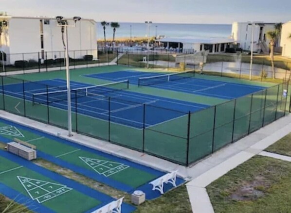 A tennis court with a net, surrounded by a fence, and adjacent to a building.