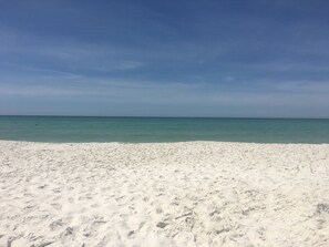 A beach with white sand and a calm sea under a clear sky.
