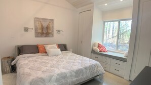 Una camera da letto con un letto grande, una panchina finestrata vista alberi e un quadro appeso al muro.