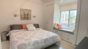 A bedroom with a large bed, a window seat with a view of trees, and a painting on the wall.