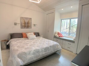 Un dormitorio con una cama grande, un asiento junto a la ventana con vistas a árboles y un cuadro en la pared.