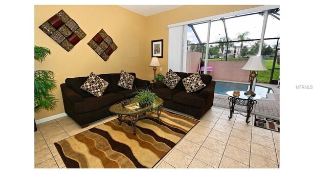 A living room with two sofas, a coffee table, a lamp, and a view of a swimming pool. - 3 Bedroom,3 Bath Townhouse in Gate Resort (Kissimmee)