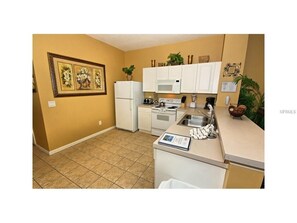 Kitchen features a microwave, stove, and sink, with a small island and artwork on the wall.