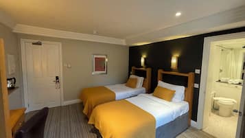 A hotel room with two beds, a desk, a chair, a door, and a bathroom visible through an open door.