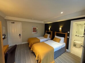 A hotel room with two beds, a desk, a chair, a door, and a bathroom visible through an open door. - Shandon House (Richmond)