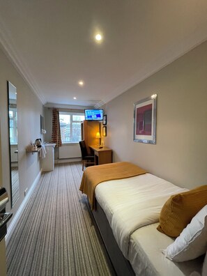 A hotel room with a bed, a desk with a computer, a chair, a small table with a lamp, a window with curtains, and a television on a stand. - Shandon House (Richmond)
