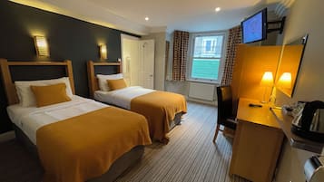 A hotel room with two beds, a desk with a chair, a TV, and a window with curtains.