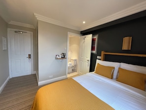 A hotel room with a bed, a bedside table, a nightstand, a wall-mounted shelf, and a door. - Shandon House (Richmond)