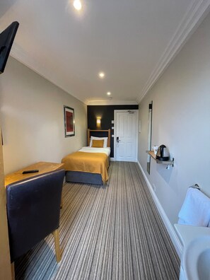 A hotel room with a bed, a desk, a chair, a bathroom, and a small shelf with a kettle. - Shandon House (Richmond)