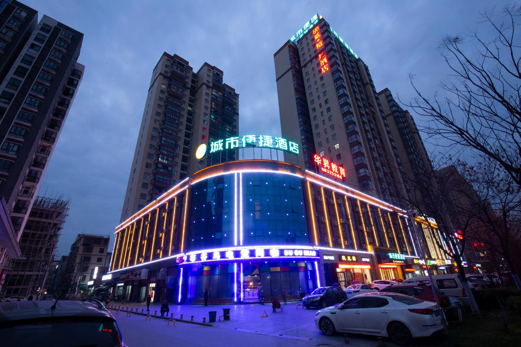 A multi-story hotel with illuminated signage, a parking lot, and surrounding high-rise buildings.