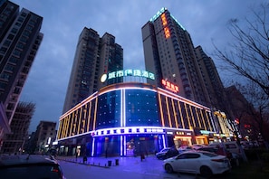 A multi-story hotel with illuminated signage, a parking lot, and surrounding high-rise buildings. - City Comfort Inn Xiantao First Middle School (Xiantao)