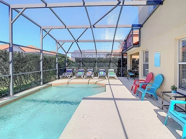 A swimming pool with a glass enclosure, surrounded by lounge chairs and a patio area.