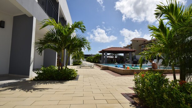 A pool area with palm trees, a covered seating area, and a building with balconies.