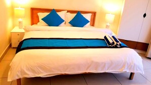 A double bed with a wooden headboard, white bedding, and blue accent pillows. There are two bedside tables with lamps and a small nightstand.