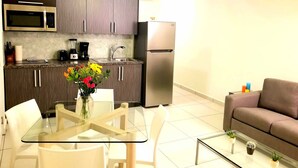 A modern kitchen with a microwave, coffee maker, and refrigerator. There is a dining table with chairs and a vase of flowers.