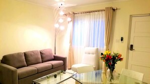 A living room with a glass-top coffee table, a sofa, a white armchair, and a dining table with chairs.