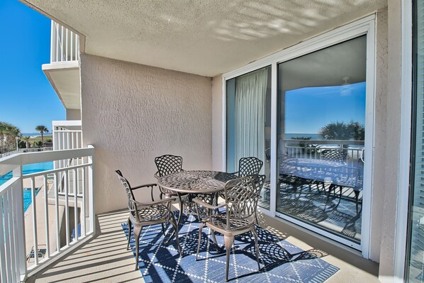 A balcony with a table and chairs, a view of the pool, and a glass door leading to the outdoors.