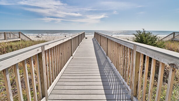 Une promenade en bois qui mène à une plage, avec un ciel dégagé.
