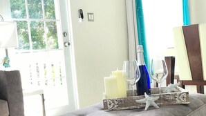 A living room with a grey sofa, a wooden side table with candles and starfish, a blue vase, and a glass of water. - Luxe Villa With Amazing Private Pool For 22 Guest (Manatí)