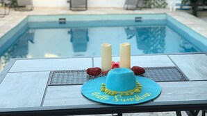 A poolside table with a blue hat and candles. - Luxe Villa With Amazing Private Pool For 22 Guest (Manatí)