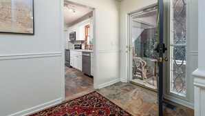 A hallway with a patterned rug, a kitchen in the background, and a glass door with a decorative metal frame. - •Newly redecorated cozy cabin close to town• (Highlands)