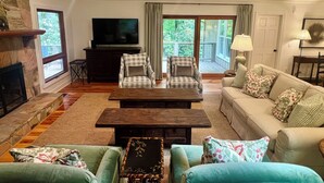 A living room with a fireplace, a television, a sofa, a coffee table, and a balcony with a view of trees. - •Newly redecorated cozy cabin close to town• (Highlands)