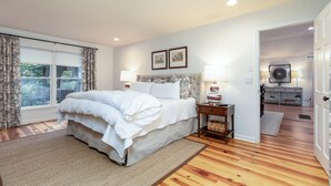 A bedroom with a large bed, two bedside lamps, a nightstand, a wooden floor, and a view of the outdoors through a window with curtains. - •Newly redecorated cozy cabin close to town• (Highlands)
