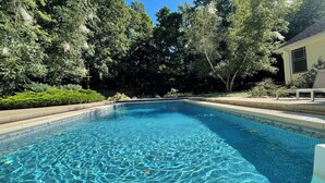 A rectangular swimming pool with clear blue water, surrounded by lush greenery and a white building with a window. - Secluded retreat Heated pool 13 acres pool table playground (Union Pier)