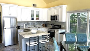 A modern kitchen with white cabinets, a stainless steel refrigerator, a microwave, and a gas stove. There is a large island with a bowl and two bar stools. - Secluded retreat Heated pool 13 acres pool table playground (Union Pier)