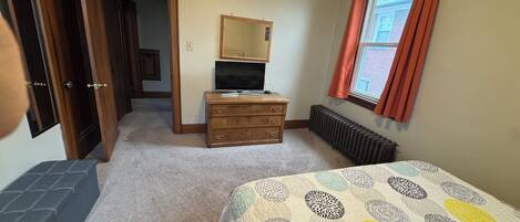 Un dormitorio con cama, cómoda, televisor y ventana con cortinas.