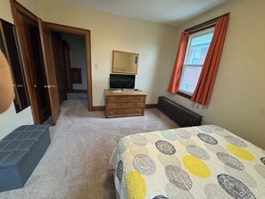 A bedroom with a bed, dresser, TV, and a window with curtains.