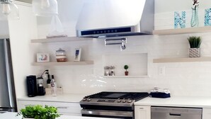 A modern kitchen with a central island, stainless steel appliances, and wooden stools. - Luxury Cottage w/ Bay & Boardwalk Views--steps from the water (North Beach)