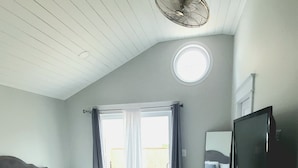A bedroom with a bed, a ceiling fan, a TV, and a window with curtains. - Luxury Cottage w/ Bay & Boardwalk Views--steps from the water (North Beach)